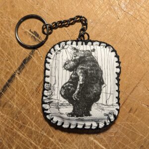 A handmade keychain from canvas with a printed illustration drawing of a Hippo in the shower by an artist Žilvinas Bražukas Production – Rankų darbo raktų pakabukas iš drobės su atspausdinta iliustracija -Begemotu duše