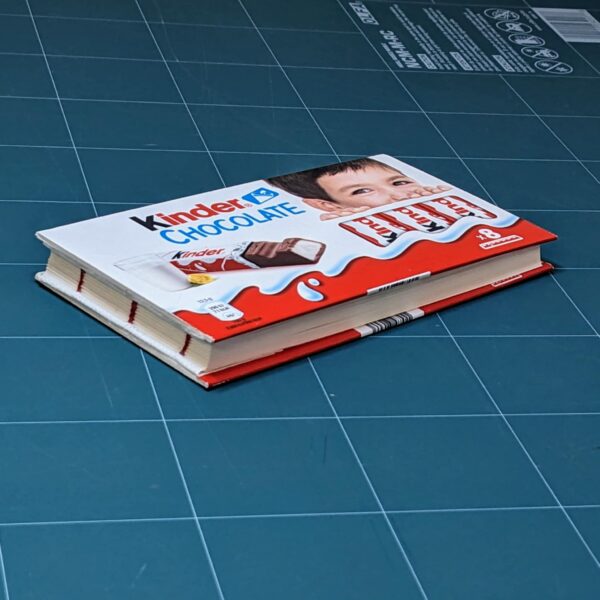 Handmade notebook with upcycled cover of Kinder chocolate package binded by an artist Žilvinas Bražukas Production. Rankų darbo užrašinė su pernaudota Kinder Šokolado pakuote
